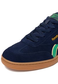 Marineblaue Wildledersneaker mit grünen und gelben Akzenten, ausgestattet mit einer hellbraunen Gummisohle und traditioneller Schnürung.