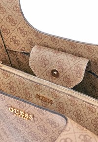 Borsa a mano color sabbia con un pattern testurizzato, dotata di dettagli in oro e logo. Include una tasca con zip e un compartimento con patta a scatto.