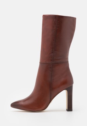 Brun læderstøvle, midt på læggen, med spids tå og høj blokhæl, glat finish og synlige sømdetaljer.