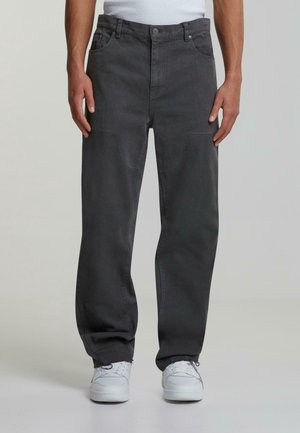 Grau Denim-Hosen mit lockerer Passform, Fünf-Taschen-Design, sichtbaren Nähten und subtiler Textur. Getragen mit weißen Sneakers.