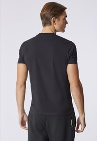 T-shirt nero a maniche corte con una texture in cotone morbido. Presenta un collo a giro e dettagli minimi sul retro.