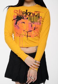 Long-sleeve, cropped yellow shirt with black and pink graphic print. Paired with a black skirt featuring a flared design and visible seams.