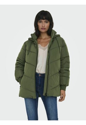 Veste matelassée vert olive avec un design ajusté, fermeture éclair à l'avant, capuche ajustable et poches latérales, associée à un haut léger et un jean bleu.