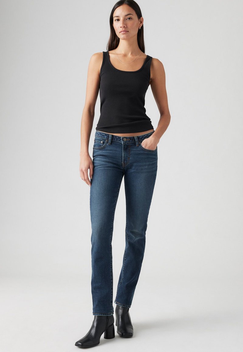 Top nero abbinato a jeans blu a gamba dritta. I jeans presentano una vita a media altezza e il modello indossa stivaletti neri con tacco.