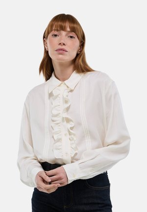 Blouse blanche à manches longues avec un devant à volants, fermeture à boutons et col structuré. Présente des détails de pinces discrètes le long de la patte de boutonnage.