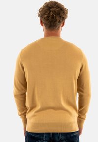 Gelber gestrickter Pullover mit langen Ärmeln und einem runden Ausschnitt, der eine glatte Textur sowie gerippte Bündchen und einen gerippten Saum aufweist.