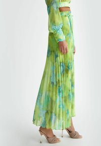 Gonna maxi plissettata di un vivace verde con motivi ad acquerello blu, realizzata in tessuto leggero. Presenta una vita alta e una texture liscia.