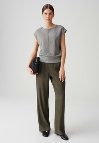 Grijze T-shirt met korte mouwen in een losse pasvorm en subtiele glans, gecombineerd met olijfgroene geplooide wijde broek. Zwarte clutch met witte accenten.