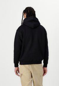 Schwarzer Kapuzenpullover aus weichem Material, mit lässiger Passform und gerippten Bündchen, kombiniert mit beigen Cargo-Hosen.