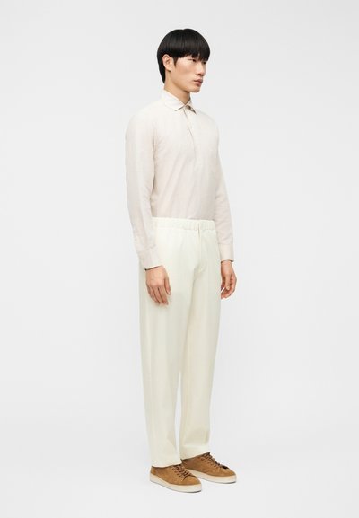 Ανοιχτό μπεζ πουκάμισο μακρυμάνικο με γιακά, σε συνδυασμό με λευκό παντελόνι με ελαστική μέση και καφέ αθλητικά παπούτσια. Μίνιμαλ σχεδιασμός και χαλαρή γραμμή.