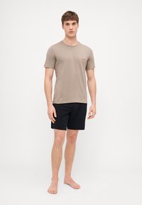 T-shirt en coton beige à manches courtes et logo rouge, associé à un short noir. Design simple, coupe ajustée, aspect décontracté.