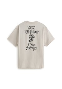 Camiseta de algodón beige con texto gráfico en negro "VANS 'OFF-THE-WALL'" y un personaje de dibujos animados, con mangas cortas y diseño de cuello redondo.