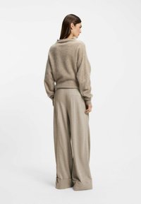 Beige, fluffy sweater with a low neckline and dropped shoulders, paired with high-waisted, wide-leg trousers in a matching light beige.