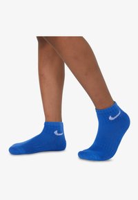 Puha, texturált anyagból készült kék bokaszakáll, amelyen a fehér Nike logó a külső oldalon található. Könnyű és rugalmas kialakítás.