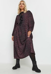 Pitkä, löysä mekko, jossa on violetti ja musta leopardi-printti, ja jossa on rypytetty musta nauha kaula-aukossa ja puffimaiset hihat.