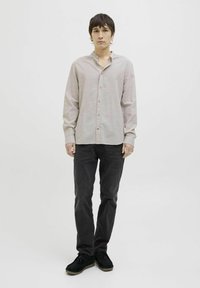 Camisa de botones rosa claro con cuello de banda, mangas largas y una textura sutil, combinada con jeans gris oscuro y calzado negro.