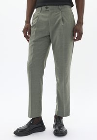 Pantalones a cuadros verdes con corte entallado, que cuentan con pinzas frontales y cierre de un solo botón, combinados con mocasines negros.