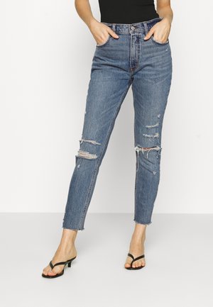 Blå denim jeans med høj talje, slidte detaljer og frynset kant. Stoffet har en klassisk tekstur med synlige stikninger.