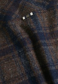 Ulltyg i mörkblått med brunt och grått rutmönster. Har en liten svart och vit etikett, texturerad yta med en mjuk finish.