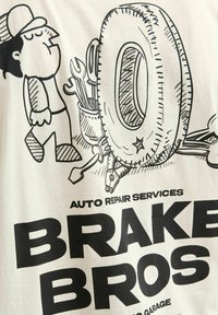 Hvid t-shirt med et sort tegneserie design af en mekaniker, et dæk, unbrako-nøgle og fed tekst med teksten "BRAKE BROS AUTO REPAIR SERVICES."