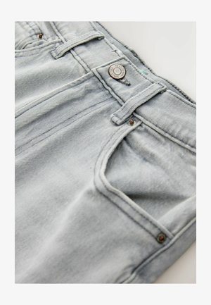 Svijetloplave traperice s izblijedjelim uzorkom, zatvaranjem na dugme i prošivenim prednjim džepovima. Istaknuto je vidljivo šivanje i metalni detalji.