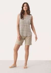 Blusa sin mangas de color gris claro con un patrón y un sutil escote en V, combinada con pantalones cortos beige doblados y chanclas blancas.