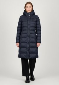 Piumino blu navy con cappuccio, design trapuntato, bottoni a pressione e patch del logo. Arriva a metà polpaccio con maniche lunghe. Texture liscia.