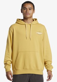 Yellow hoodie with a front pocket and drawstrings. Features a small logo on the left chest. Made of soft fabric; slightly oversized fit.