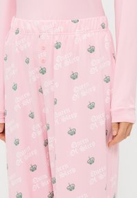 Calças de pijama rosa claro com uma textura suave, apresentando um padrão repetido de coroas e "Rainha do Sono" em branco e verde. Inclui uma cintura com botões.