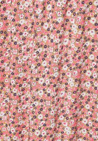 Blommigt tyg med små vita, rosa och marinblå blommor på en beige bakgrund, med en texturerad väv och veckad design.