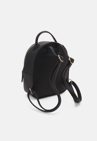 Sac à dos noir en matériau lisse, doté d'une forme arrondie, d'une fermeture éclair dorée, de deux bretelles réglables et d'une poignée supérieure pour le transport.