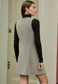 Abito con motivo pied de poule, corpetto aderente e gonna svasata, realizzato in tessuto dalla consistenza liscia. Maniche lunghe nere a coste.