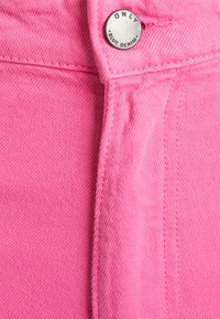 Tecido de denim rosa com um botão com a inscrição "ONLY BLUE DENIM", costura visível e um acabamento texturizado.