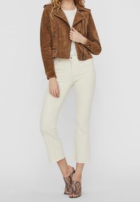 Bruine suède cropped jacket met ritszakken en drukknoopsluiting, gecombineerd met crèmekleurige cropped broeken en open-toe hakken met slangenprint.