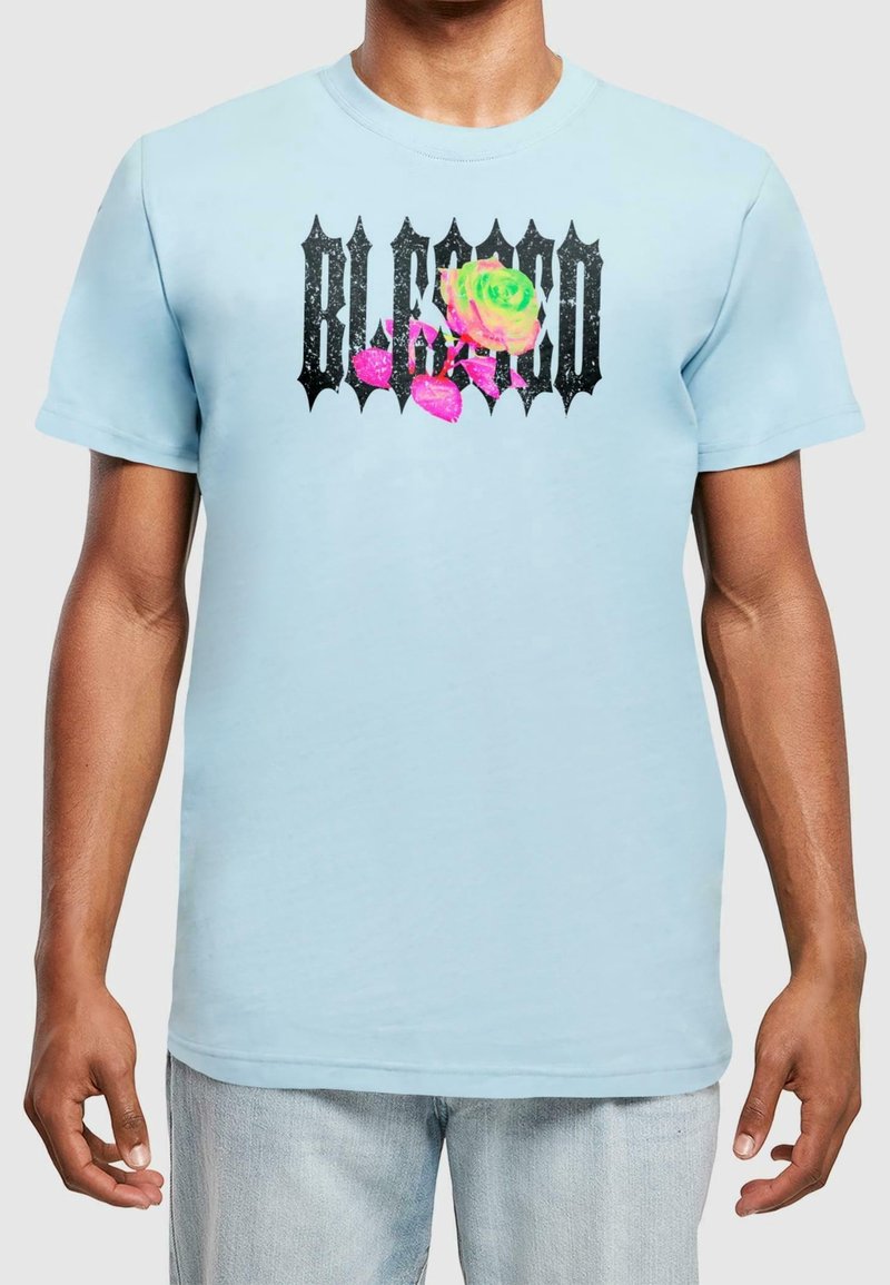 T-shirt en coton bleu clair avec un graphique noir portant le mot "BLESSED" et un design de rose colorée avec des feuilles roses. Manches courtes.