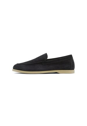 Mocassin sans lacets en daim noir avec semelle en caoutchouc beige, petit talon et couture de style mocassin sur fond blanc.