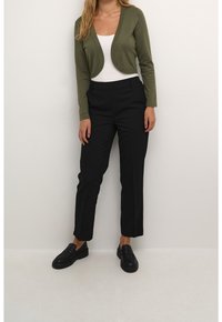 Un cardigan court vert olive sur un top blanc, associé à un pantalon noir sur mesure et des mocassins noirs. Textures lisses, design moderne.