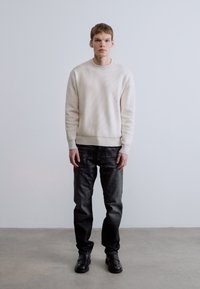 Fehér bordázott kötött pulóver, sötét farmer és fekete cipő. A szett klasszikus kialakítású, texturált pulóverrel és testhezálló nadrággal.