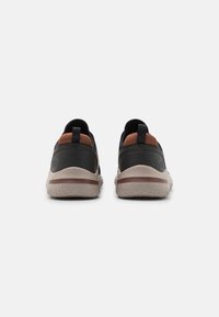 Schwarze Sneaker mit braunen Akzenten, ausgestattet mit einem glatten Obermaterial, gepolsterter Schuhkragen und einer strukturierten beige Laufsohle mit einem kontrastierenden Rand.