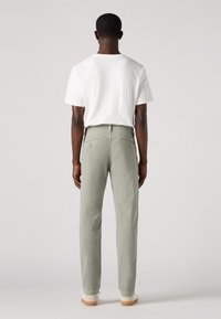 Pantaloni di cotone grigio chiaro con design a gamba dritta, dotati di tasche posteriori e una vita semplice, abbinati a una maglietta bianca semplice.