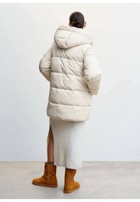 Prošívaná bunda v světle béžové barvě s horizontálním prošíváním, kapucí a volným střihem; doplněná o žebrovanou krémovou sukni a hnědé kotníkové boty.