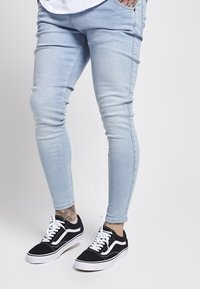 Jeans ajustados de color azul claro fabricados con denim, con una textura suave. Combinados con zapatillas de cuero negro y blanco con cordones y acabado de ante.