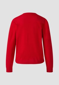 Czerwony sweter robiony na drutach z długimi rękawami, okrągłym dekoltem i ściągaczem na dole. Gładka tekstura i jednolity kolor bez wzorów czy ozdób.