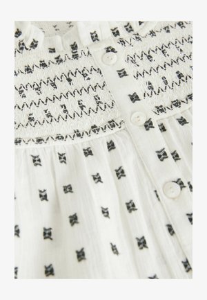 Blusa bianca con motivi ricamati neri, caratterizzata da un corpetto arricciato, apertura con bottoni e un tessuto leggero e strutturato.