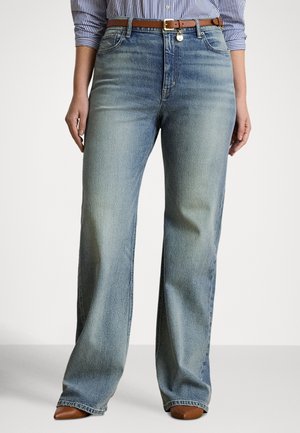 Femme portant un jean bleu clair à jambes larges, une ceinture en cuir marron, des chaussures marron pointues et une chemise rayée bleue et blanche avec les manches retroussées.