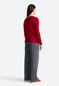 Pulover roșu din material moale, cu guler rotund și tiv ribatit. Pantaloni gri cu croi larg, asociați cu pantofi roșii cu accente albe.