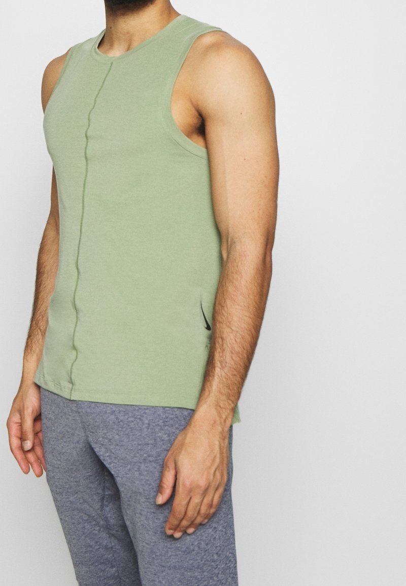 Ljusgrön ärmlös linne gjord av mjukt tyg, med en centrerad söm och subtila sidoklipp, parat med gråa träningsbyxor.