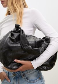 Borsa hobo in pelle nera con un design morbido, texture liscia e una cerniera di sicurezza; presenta una tracolla in pelle annodata e accessori in metallo.