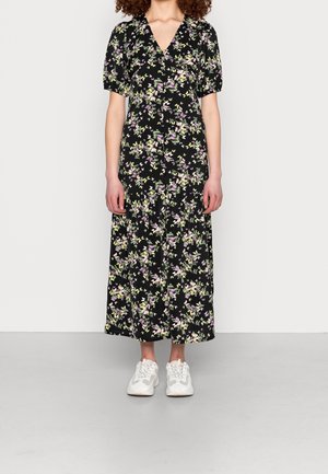 Abito midi nero a fiori con scollatura a V e maniche a sbuffo, caratterizzato da fiori viola e verdi. Abbinato a sneakers bianche.