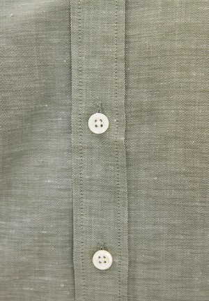 Primo piano della parte anteriore di una camicia di tessuto grigio con due bottoni bianchi a quattro fori e cuciture visibili lungo la patta dei bottoni.